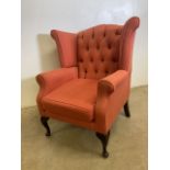 A 20th century upholstered wing back arm chair with buttoned back and Queen Anne style legs. W: