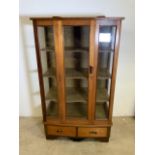 An Art Deco style glazed display cabinet with three wooden shelves and two drawers to base.