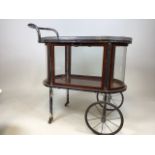 A vintage oval serving trolley/ bar cart with curved glass ends and drop down glass side doors