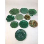 9 assorted ceramic plates and a cake stand. Various leaf patterns in green hues. Some loss