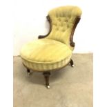 A 19th century button backed upholstered nursing chair with carved details and ceramic and brass