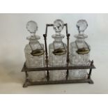 A Silver plated tantalus with three cut glass decanters with associate wine labels. W:33cm x D: