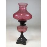 A vintage oil lamp with cranberry glass style shade - on decorative iron base. Some colour loss to