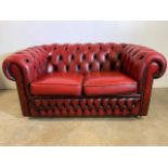 An Oxblood red leather Chesterfield two seater sofa. W:145cm x D:90cm x H:70cm