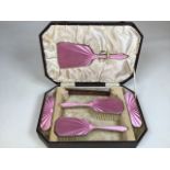 A boxed pink enamel silver backed dressing table set. Comprising hand mirror, a pair of hand brushes
