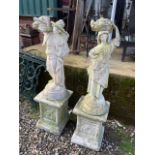 A pair of reconstituted stone garden statues on plinths of farm workers or country folk. H:120cm
