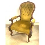 A wide seated Victorian button back arm chair with carved arms on brass and ceramic castors. W: