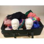 A suit case full of fabric remnants also with a pair of polystyrene heads