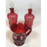 A pair of vintage cranberry glass small decanters decorated with gold flowers and a ruby glass jug