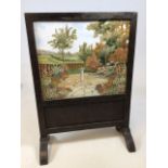 A wooden fire screen with painted and embroidered panel. Wooden stand A/F, with signs of woodworm to