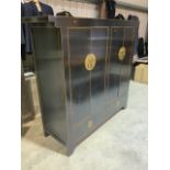 A Chinese style cupboard in black painted finish with brass fittings with four doors and two drawers