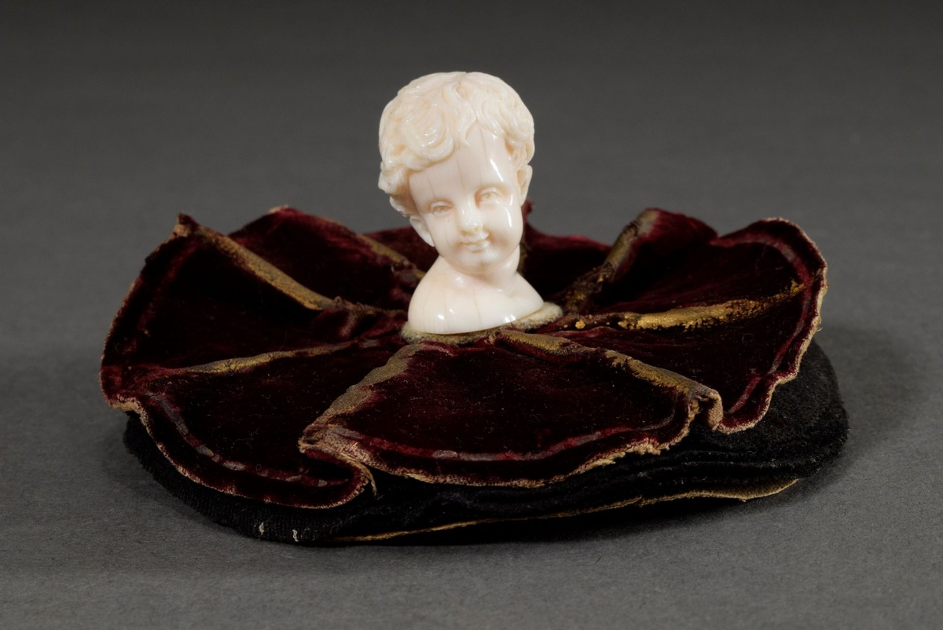 Historism ivory carving "boy's head" mounted on a round red velvet pincushion, end of 19th century,