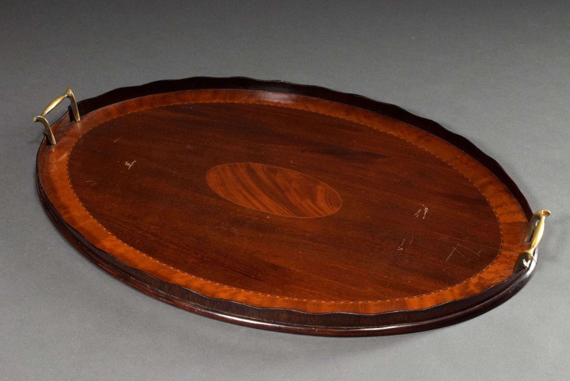 Large oval mahogany tray with ribbon inlay, brass handles on the sides and curved gallery rim, Engl