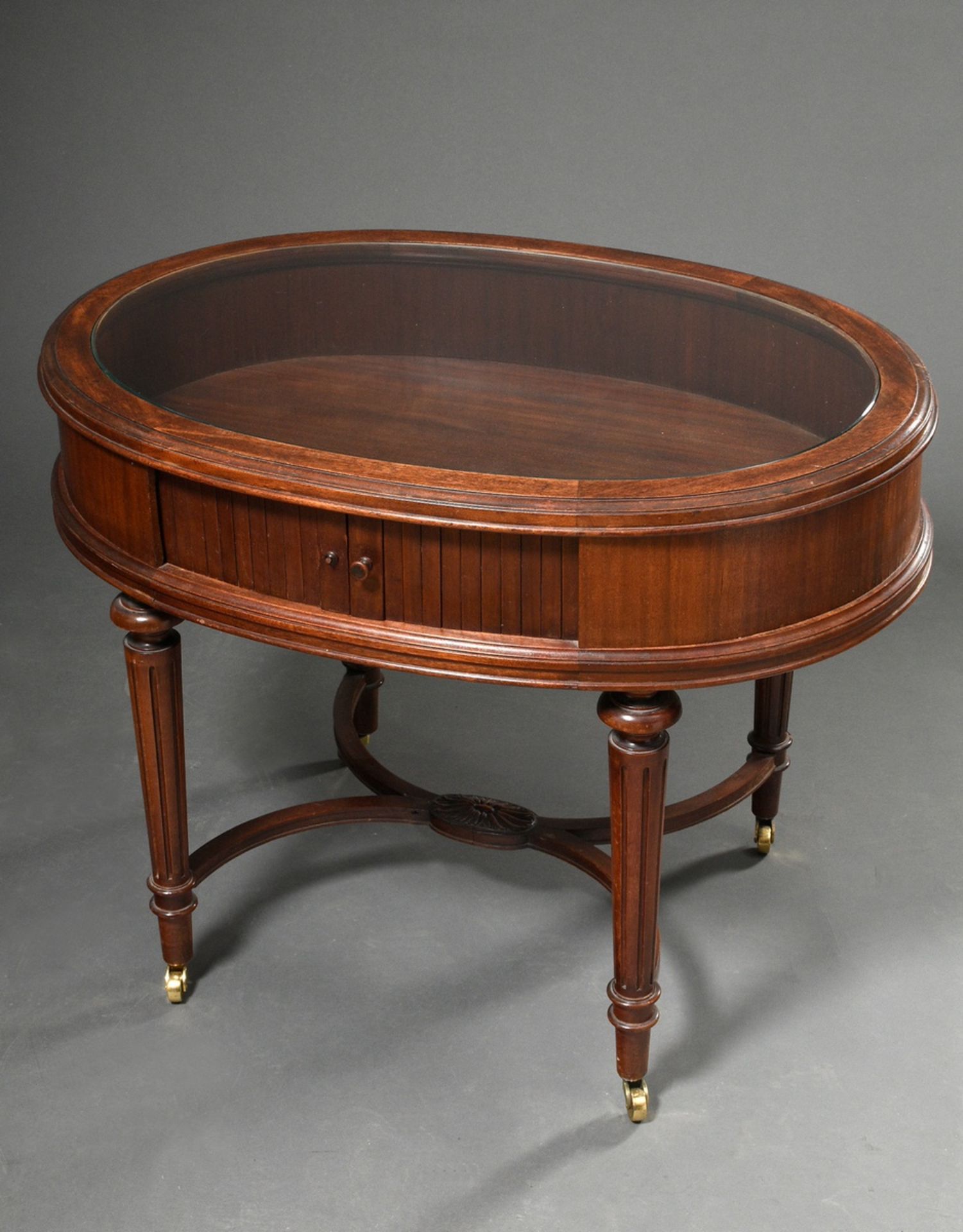 Low oval mahogany display table with glass top and side roll closure, underside signed. "Paul Tibur