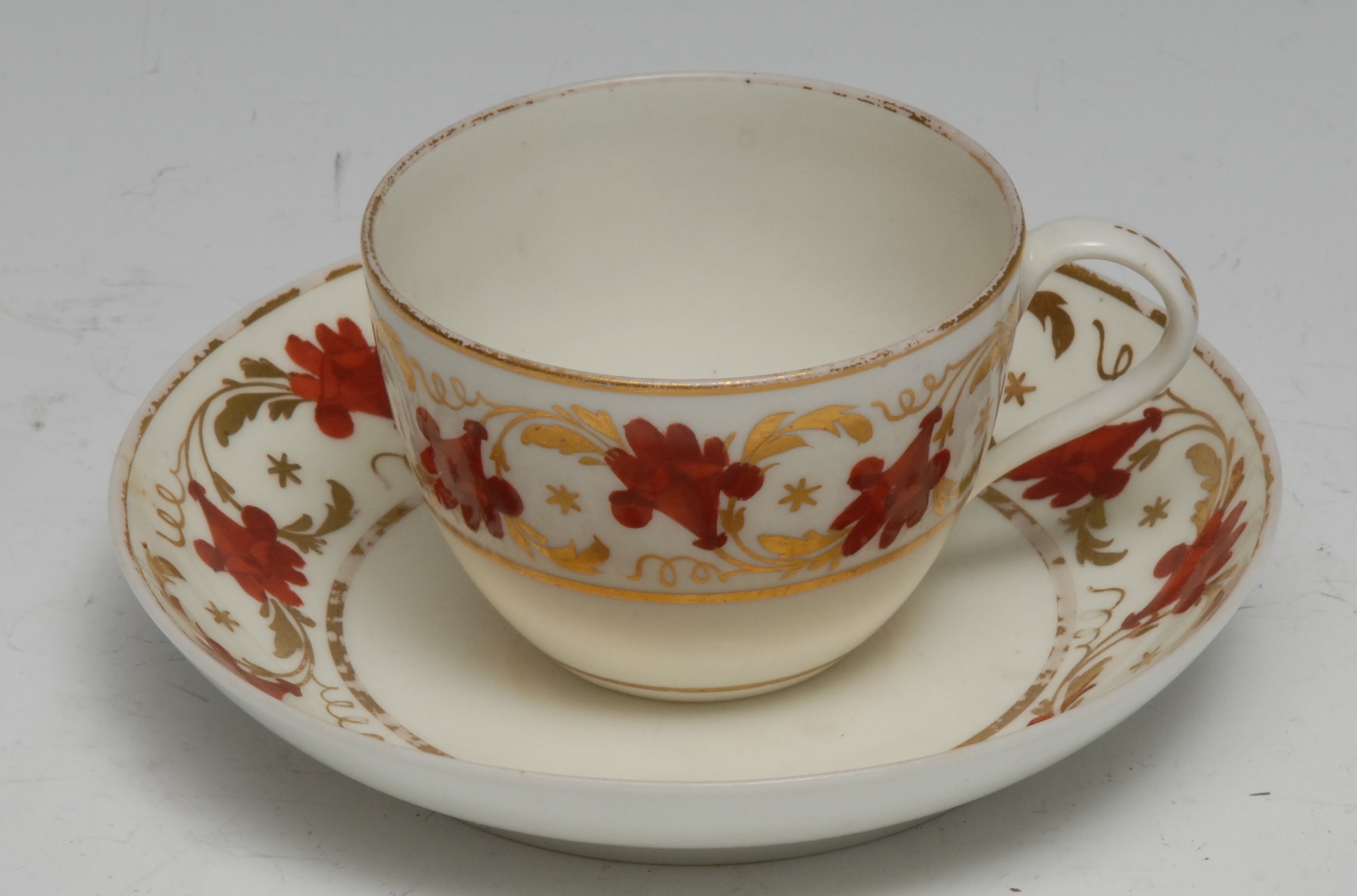 A Pinxton Bue shaped teacup and saucer, pattern no. 312, decorated in red and gilt with bands of