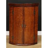 A 19th century oak wall hanging bow front corner cupboard, outswept cornice above a pair of doors