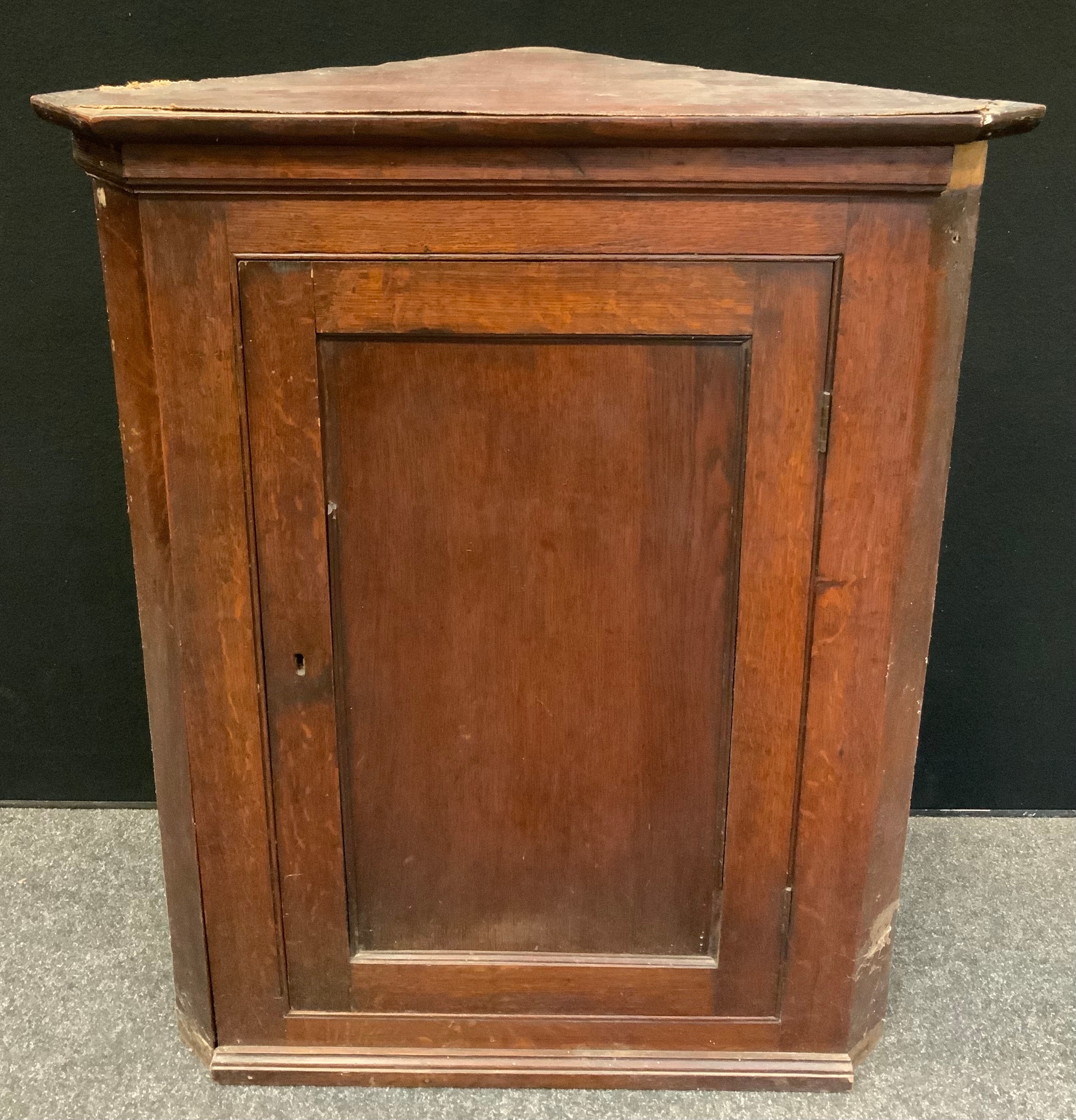 A George III oak splay front wall hanging corner cupboard, rectangular panel door enclosing two