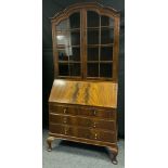 An early 20th century mahogany bureau bookcase, shaped top with a pair of glazed doors enclosing