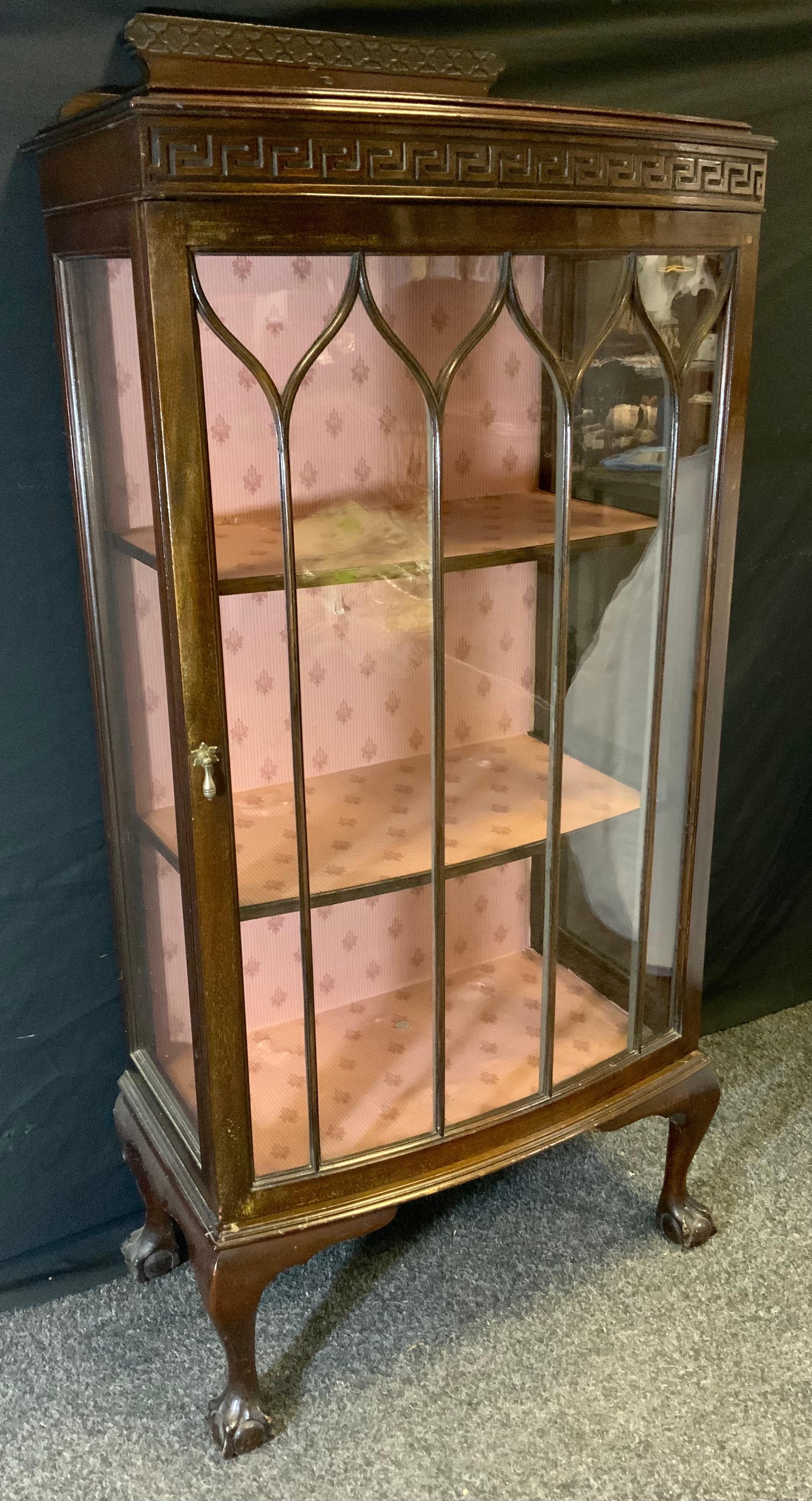 A 20th century mahogany display cabinet, shaped half gallery above a single glazed door enclosing