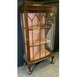 A 20th century mahogany display cabinet, shaped half gallery above a single glazed door enclosing