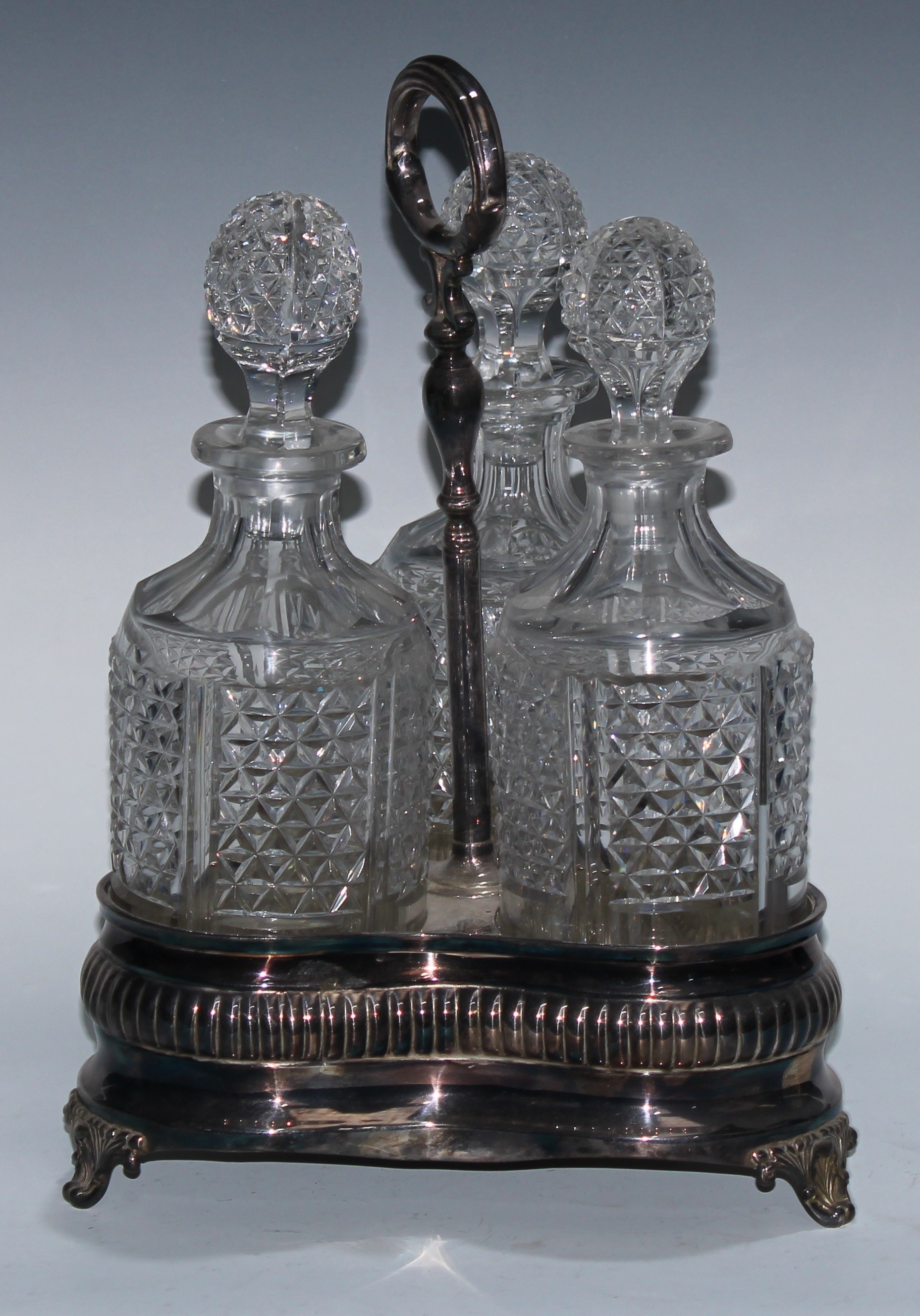 An Adam Revival EPNS and cut-glass three-bottle decanter stand, the trefoil-shaped base engraved