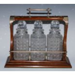 A late Victorian EPNS-mounted oak three-bottle tantalus, the unusual mechanism restraining the