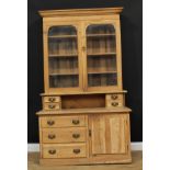 A farmhouse pine dresser, outswept cornice above a pair of glazed doors enclosing three shelves, the