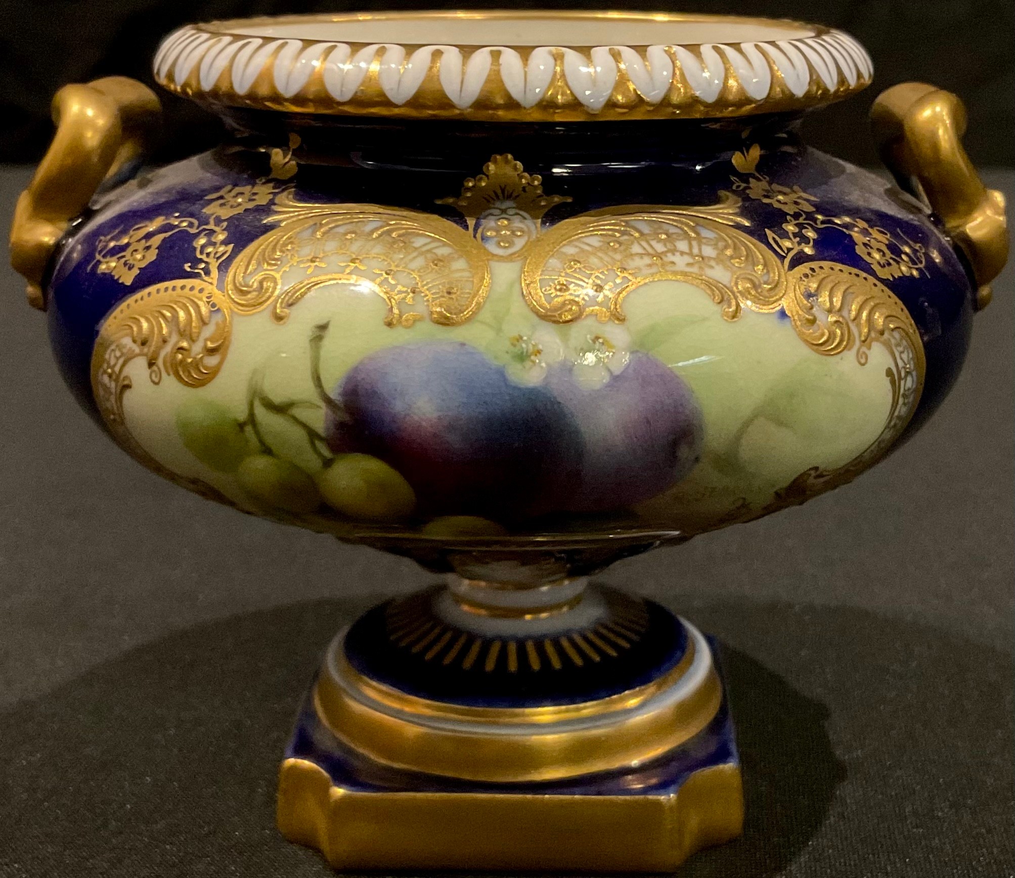 An early 20th century Royal Worcester gilded two handled pedestal urn, painted panel of fruit on