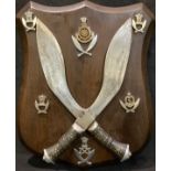 Militaria - a pair of kukri knives and Ghurka insignia mounted on wooden shield