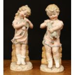 A pair of late 19th century/early 20th century German bisque figures, of a boy and girl, one holding