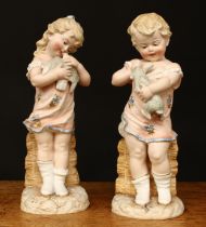 A pair of late 19th century/early 20th century German bisque figures, of a boy and girl, one holding