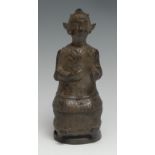 Chinese School, a patinaed bronze figure, of an ancestral deity, seated holding a mirror, wearing