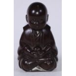 A Japanese hardwood okimono, carved as a young boy, in meditation, holding a ball, 15.5cm high,