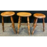 A late 19th century stool, three legs, iron bar stretcher, 53cm high; others, 47cm high (3)