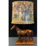 A novelty table lamp, the base with a horse, the shade with figures on horses outside a Tudor