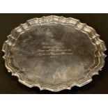 A George V silver presentation card waiter, moulded piecrust border, resting on three scroll feet,