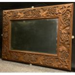 An early 20th century oak wall mirror, the frame carved in profusion with fruiting vines, bevelled