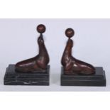 A pair of Art Deco design brown patinated bronze bookends, each cast with a seal balancing a ball,