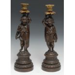 A pair of sculptural 19th century French bronzed and parcel-gilt figural candlesticks, each cast