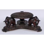 An Indian hardwood table top vase stand, the circular plateau on four elephant supports, triform