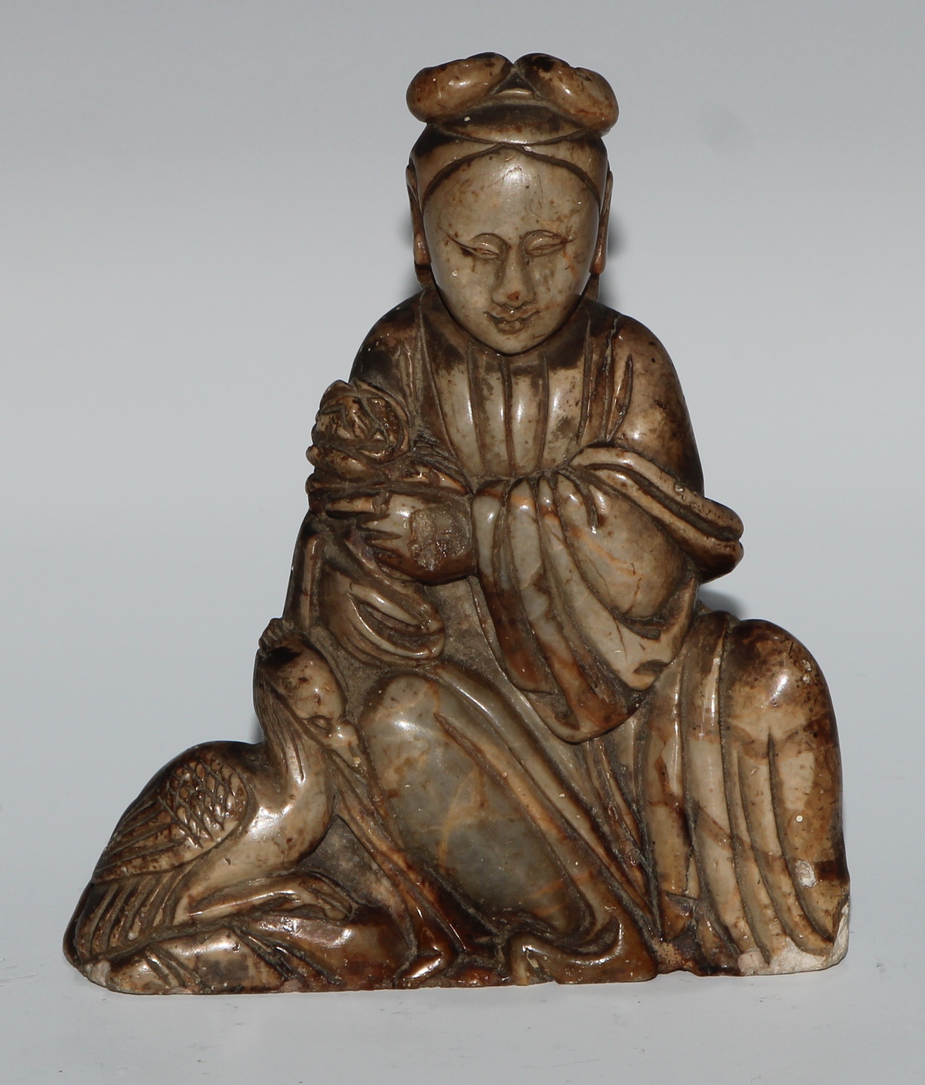 A Chinese soapstone figure, carved as guanyin, seated, serene, holding a lotus, a bird at her