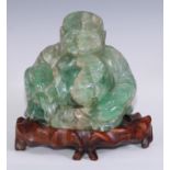 A Chinese green quartz carving, of Budai, seated, hardwood stand, 22cm high overall