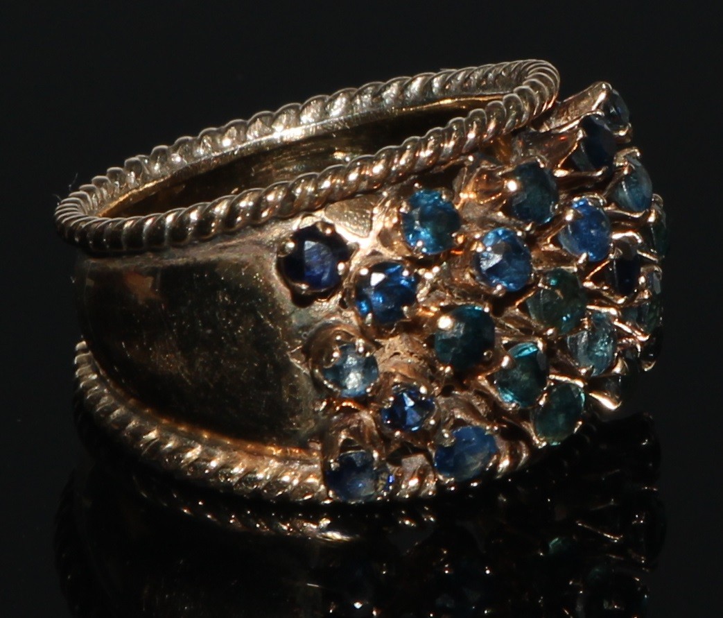 A sapphire cluster ring, arched tapering shank adorned with twenty three blue sapphires, yellow