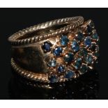 A sapphire cluster ring, arched tapering shank adorned with twenty three blue sapphires, yellow