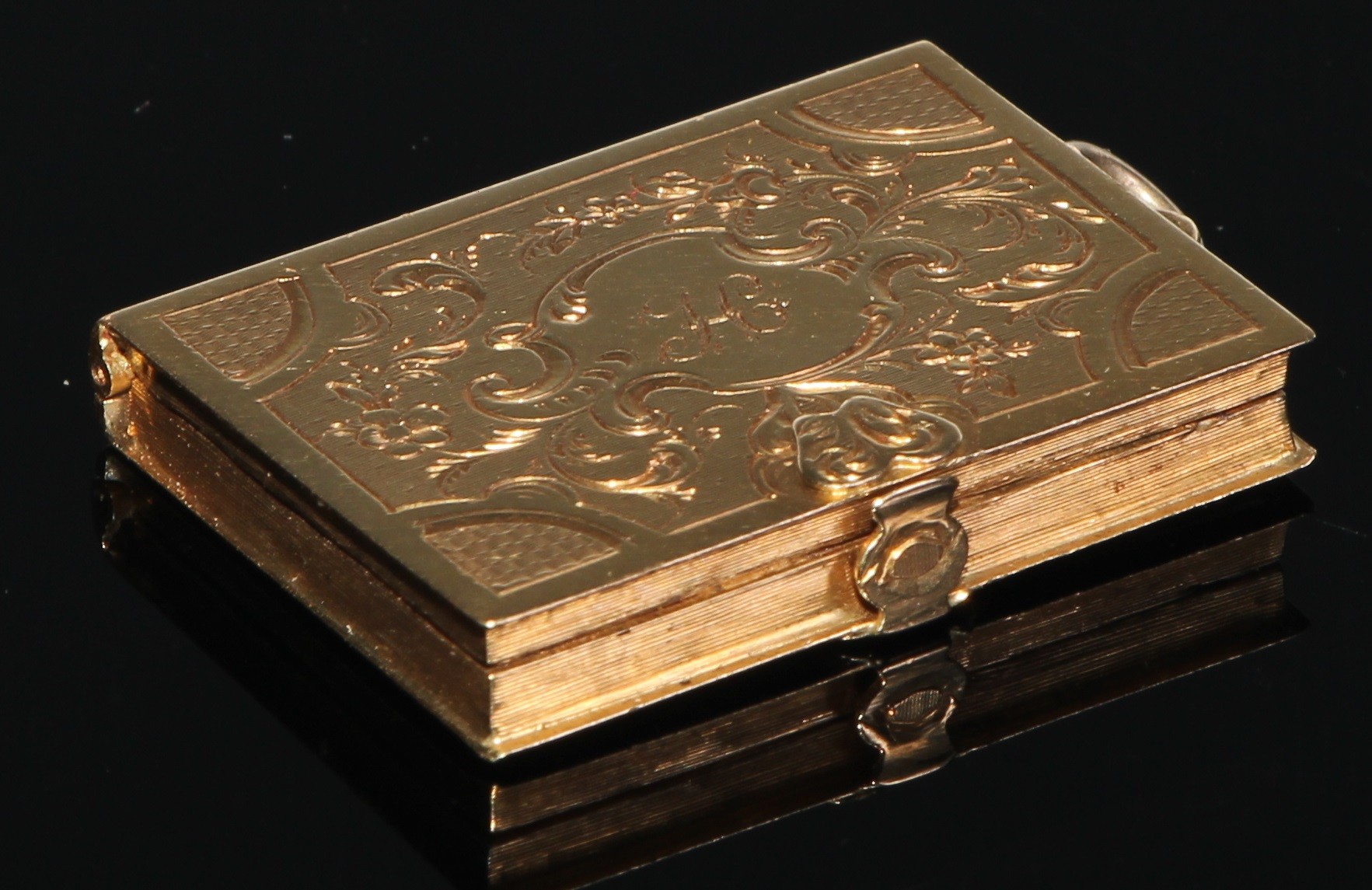 An unmarked gold vinaigrette, as a clasped book, chased and engraved with scrolling foliage,