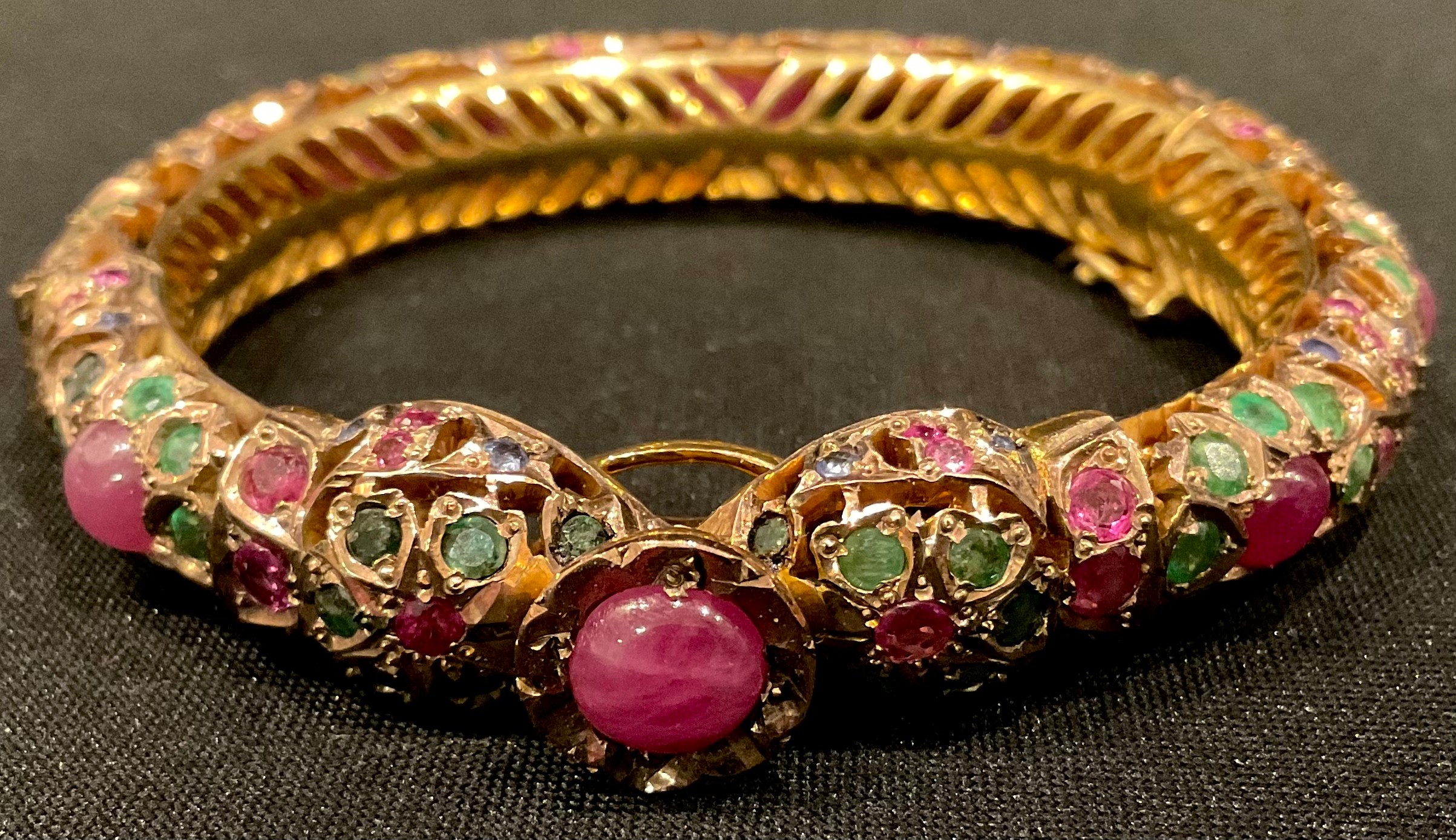 A gold plated hinged pierced openwork bangle encrusted overall with low grade cabochon rubies and