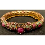 A gold plated hinged pierced openwork bangle encrusted overall with low grade cabochon rubies and