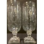 A pair of glass storm lanterns, each decorated with ovals, stepped square bases, 40cm high