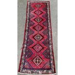 A Persian woollen runner, with seven lozenges and chevrons, geometrical border, in tones of red,