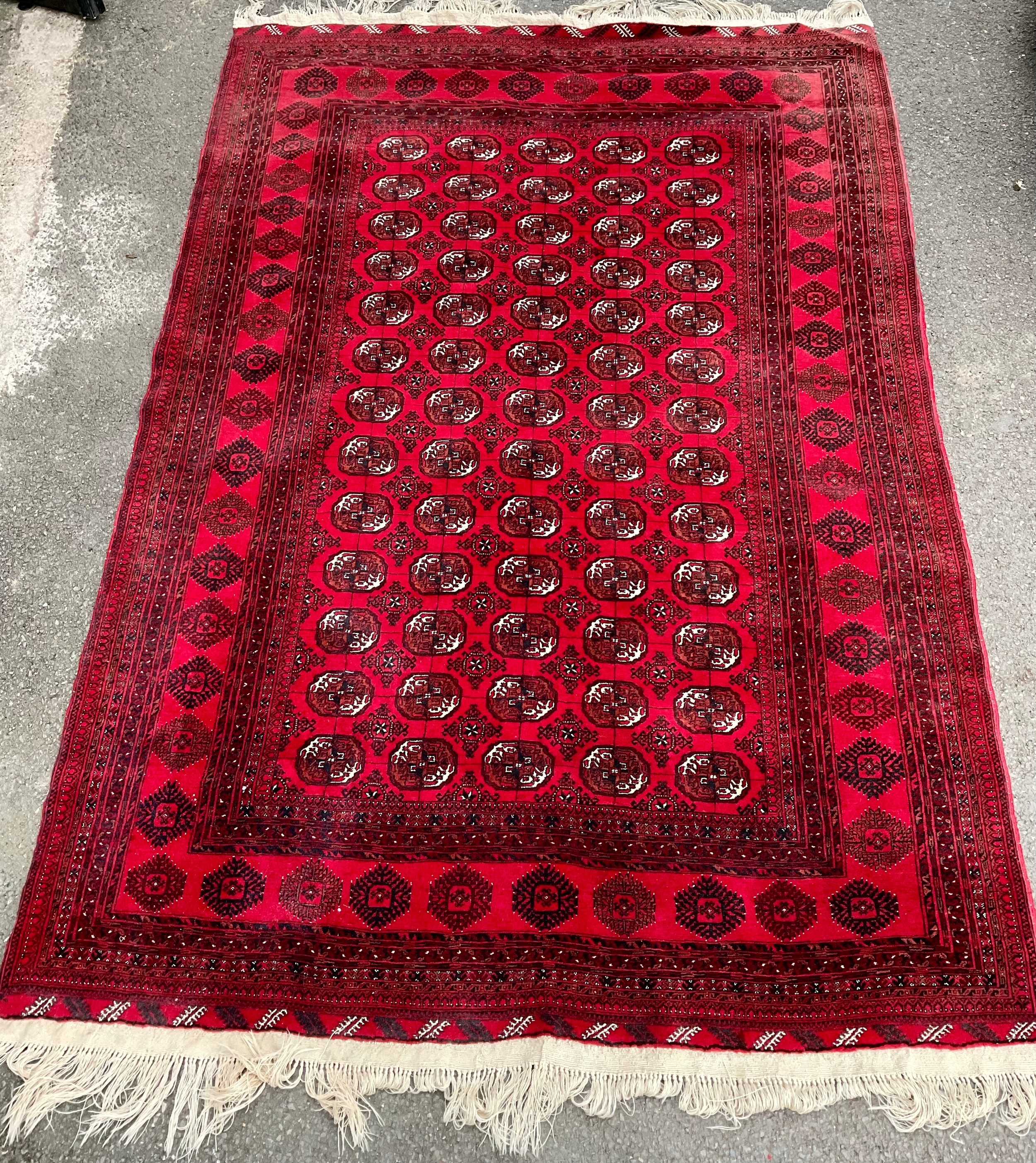 A Middle Eastern woollen rug, with five rows of guls, in tones of orange, black and white on a red